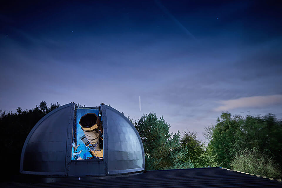night sky silhouettes of trees and dome of observatory open with the telescope peeping out