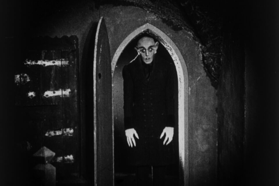 black and white photo of sinister figure standing in a gothic arched doorway