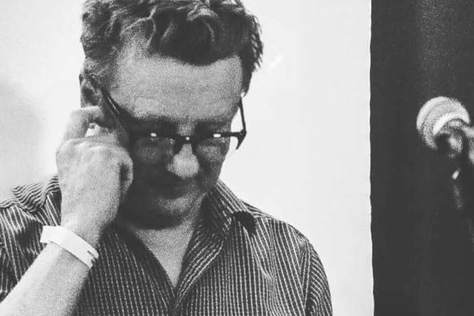 black and white photo of male looking down touching his glasses which are on his head