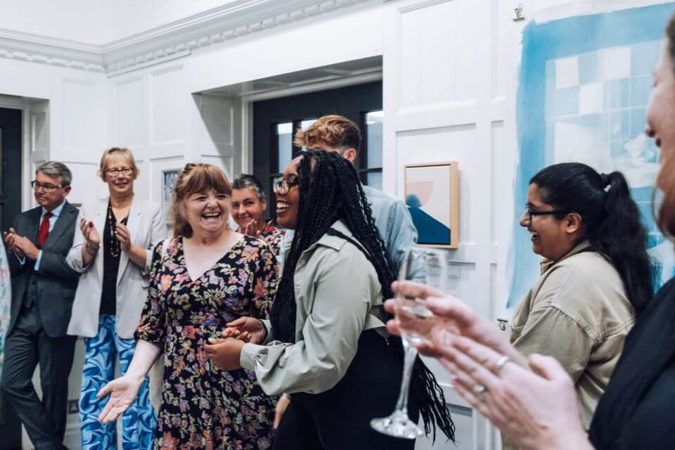 A group of people at an exhibition celebrating and clapping an artist who looks really happy.
