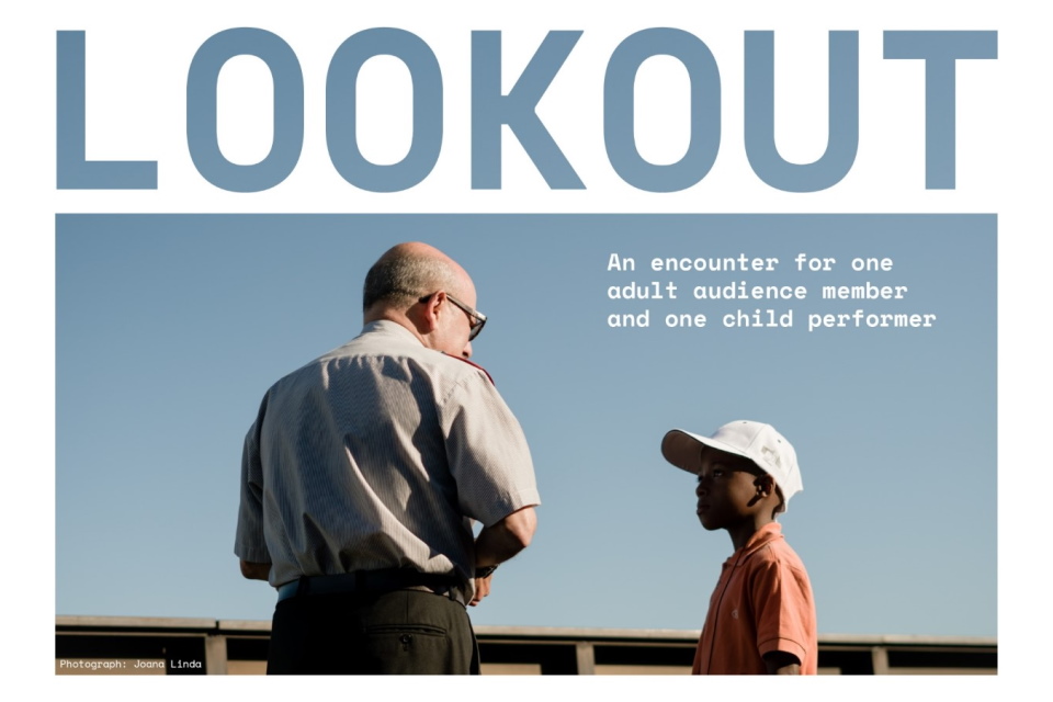 Two people, an adult and child, look out toward a blue sky with their backs toward the camera