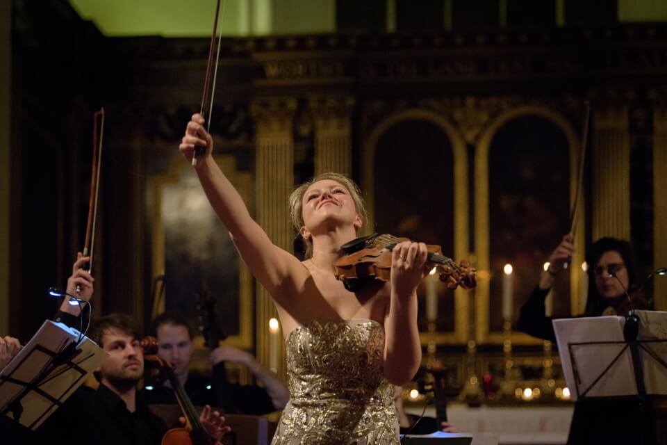 image of Harriet raising violin in the air with orchestra behind and candles