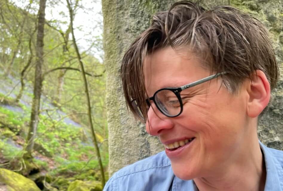 image of clare shaw looking to left and smiling wearing glasses in woodland setting