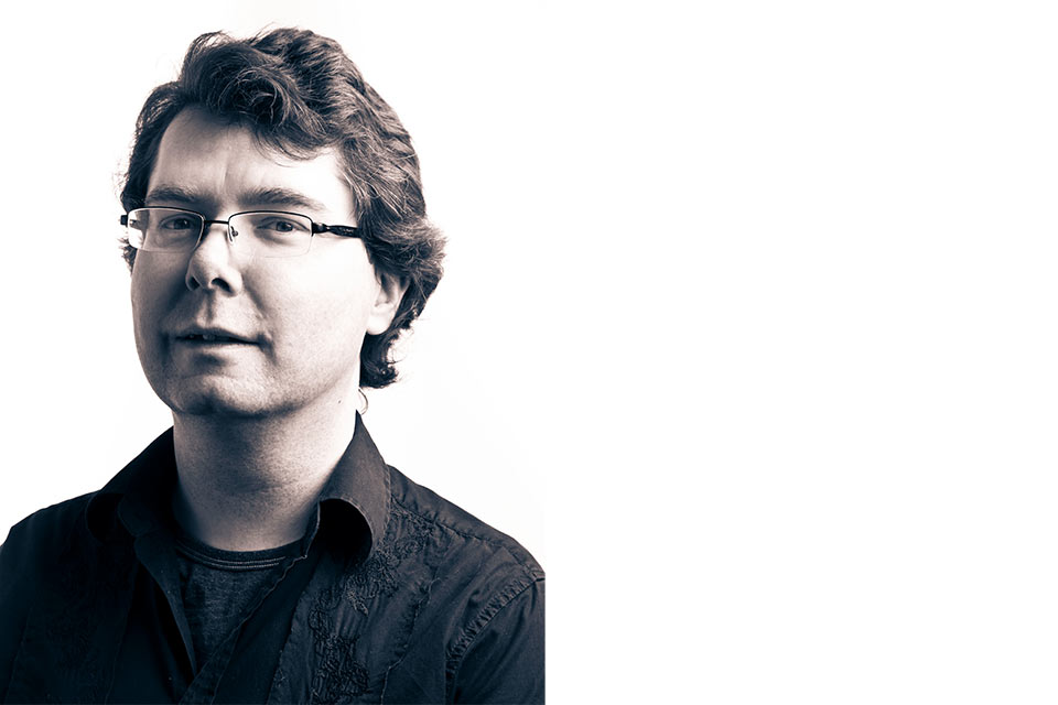 a black and white photo of a white man with glasses stares into the camera