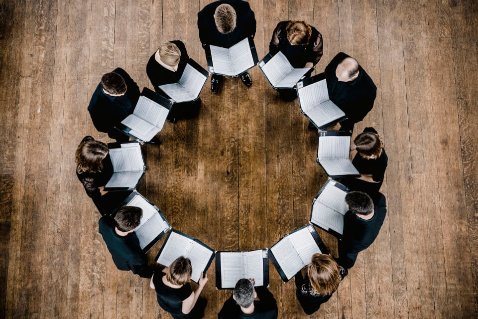 image of 12 performers holding their music and standing in a circle - view from above