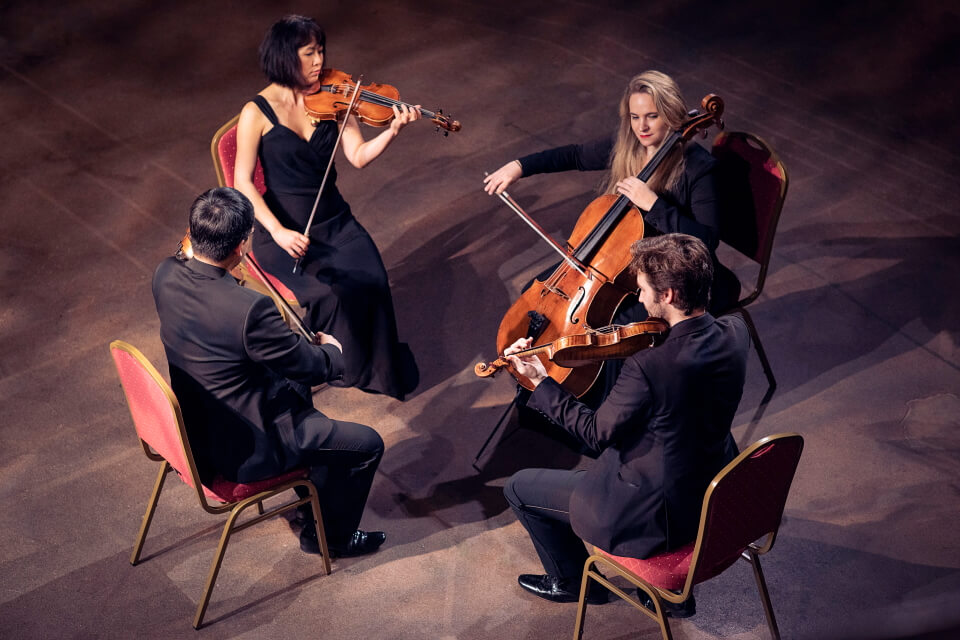 image of the four players from the quartet seated with instruments, smiling looking at each other