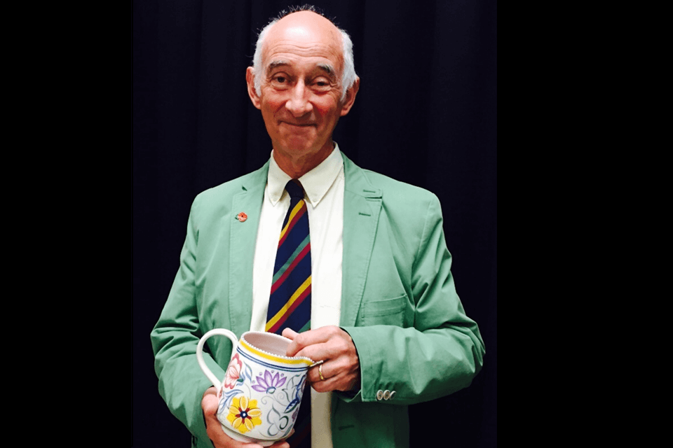 Paul Atterbury in pastel green blazer with blue and red striped tie holding a ceramic pot smiling