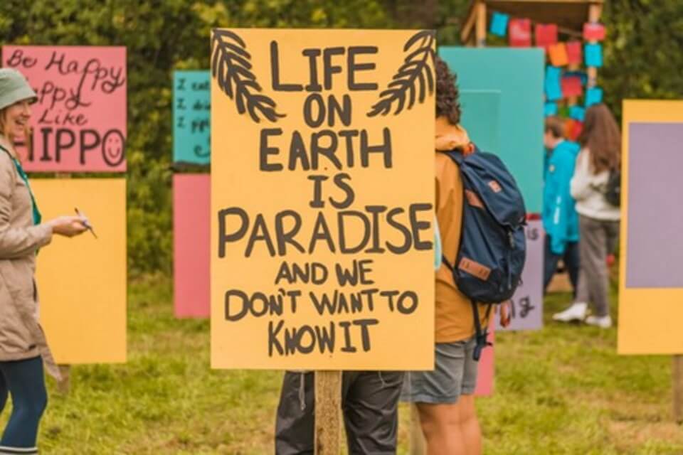 colourful placards in a field, people roaming, person to the left joyful