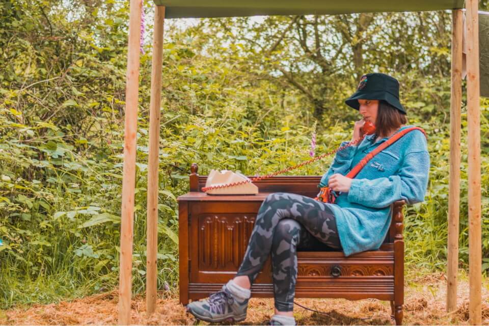 a person wearing leggings, coat and hat, sitting at wooden telephone table listening to a telephone