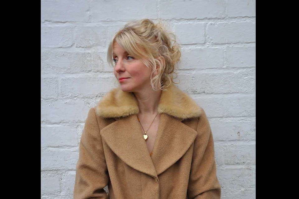 image of woman wearing camel colour jacket, blonde hair scooped up with some loose curls around face