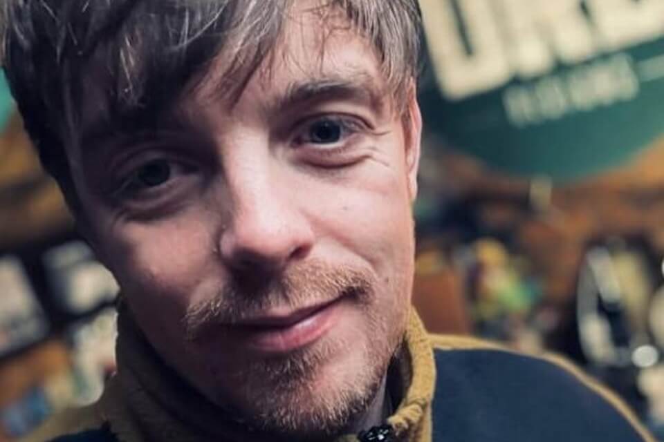 Colour photographic portrait of Dan Rhead-Brown with DRB Designs logo in background