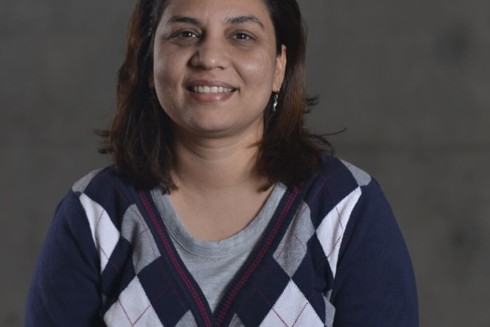 image of the female speaker smiling wearing a v-neck sweater, with long dark hair
