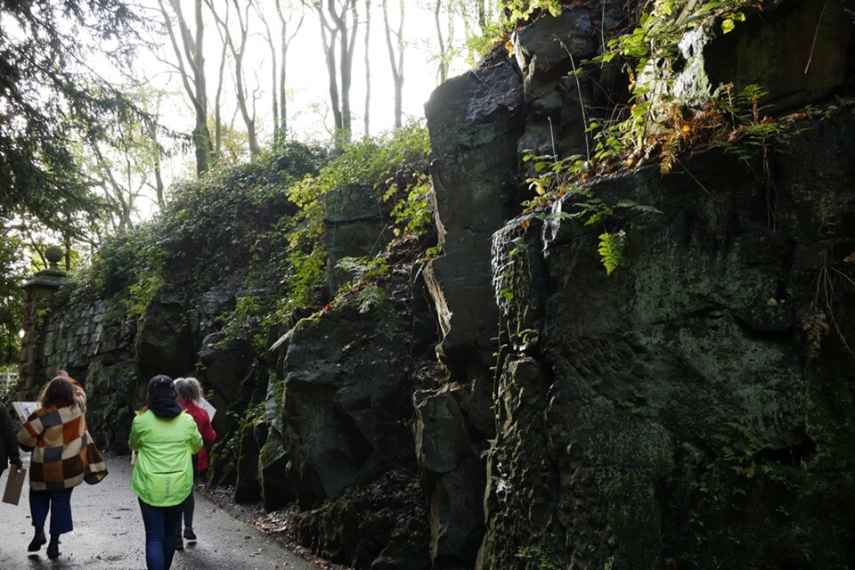 image of people walking alongside a rocky path dappled in sunlight