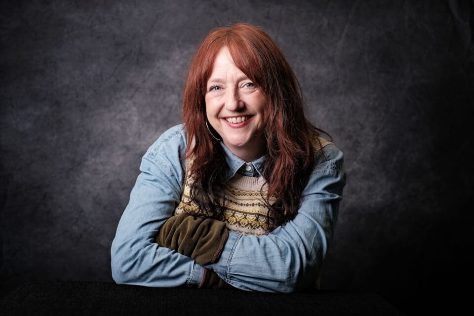 Lisa, smiling, long red hair, blue long sleeved top