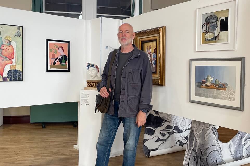 image of Malcolm at the exhibiton infront of artworks smiling