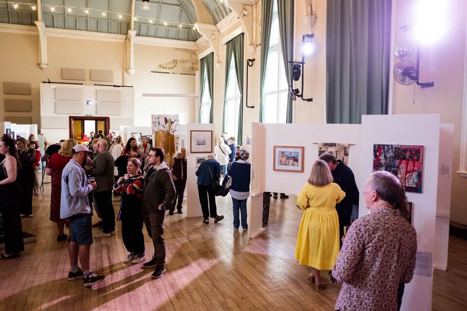 picture of people gathering an a large hall with artwork on display social scene