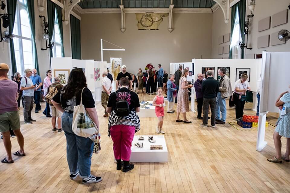 GROUP OF PEOPLE VIEWING AN EXHIBITION IN A BEAUTIFUL TOWN HALL