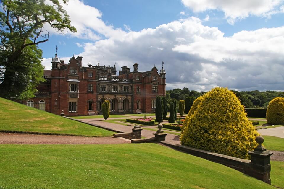 a view towards Keele Hall looking across sweeping green lawns with a blue sunny sky with clouds