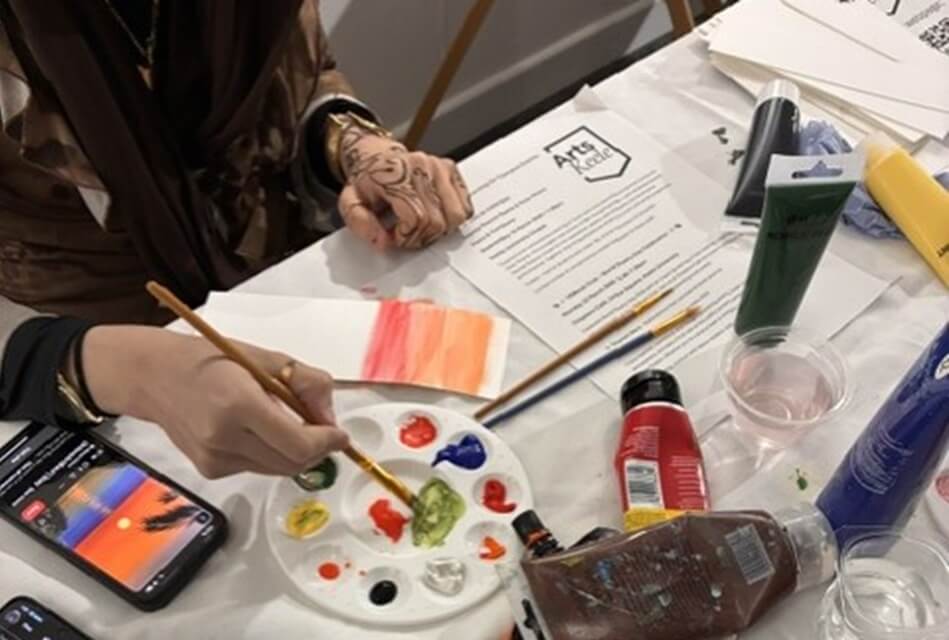 hands with paint brush next to a painting tray filled with different colours