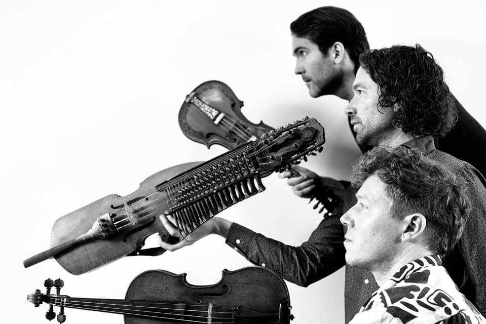 three male performers facing to the left holding their instruments alongside their faces
