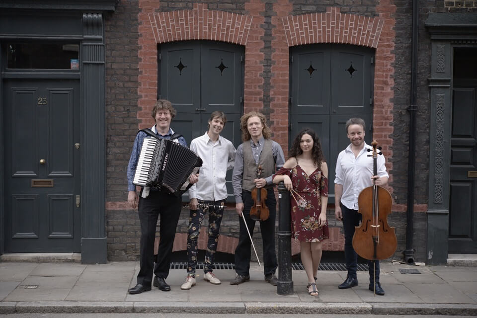 group of performers standing street side holding their instruments smiling