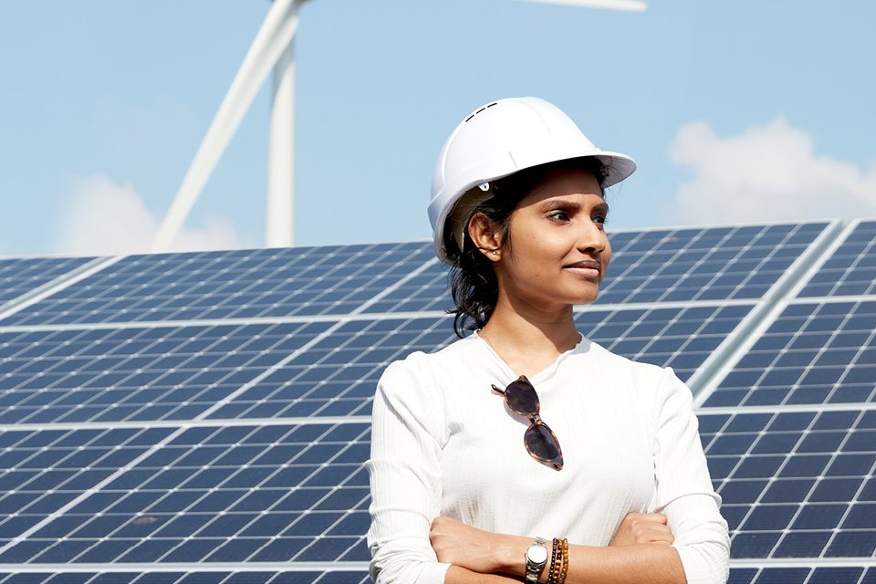 Researcher in a hard hat standing in front of solar panels and a wind turbine