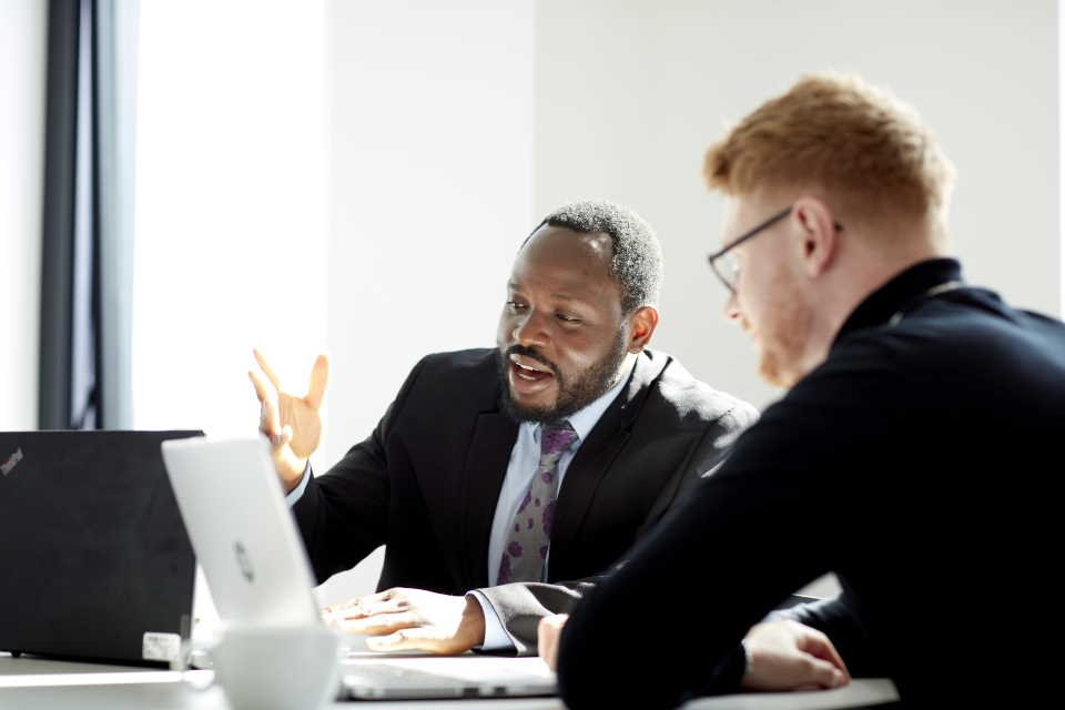 Two colleagues in discussion at a table with laptops