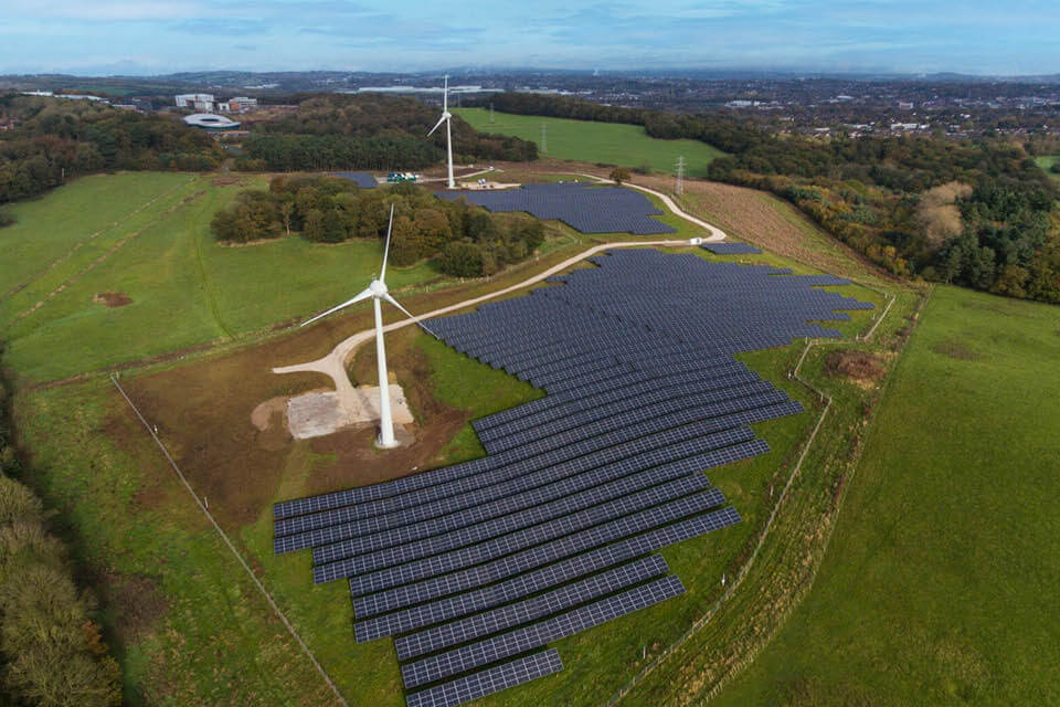 energy park with 2 wind turbines and rows of solar panels amongst fields and woodland