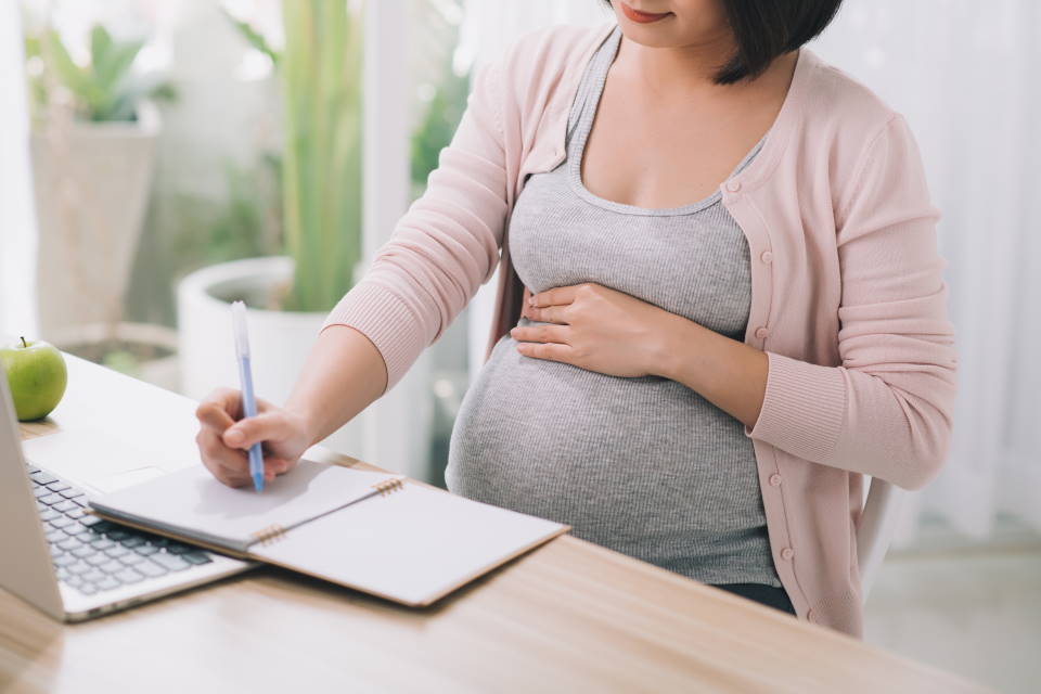 Pregnant woman sat at a table, writing notes in a notepad
