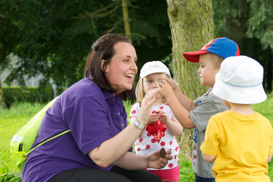 A staff member from Keele Nursery smiling and interacting with three young children