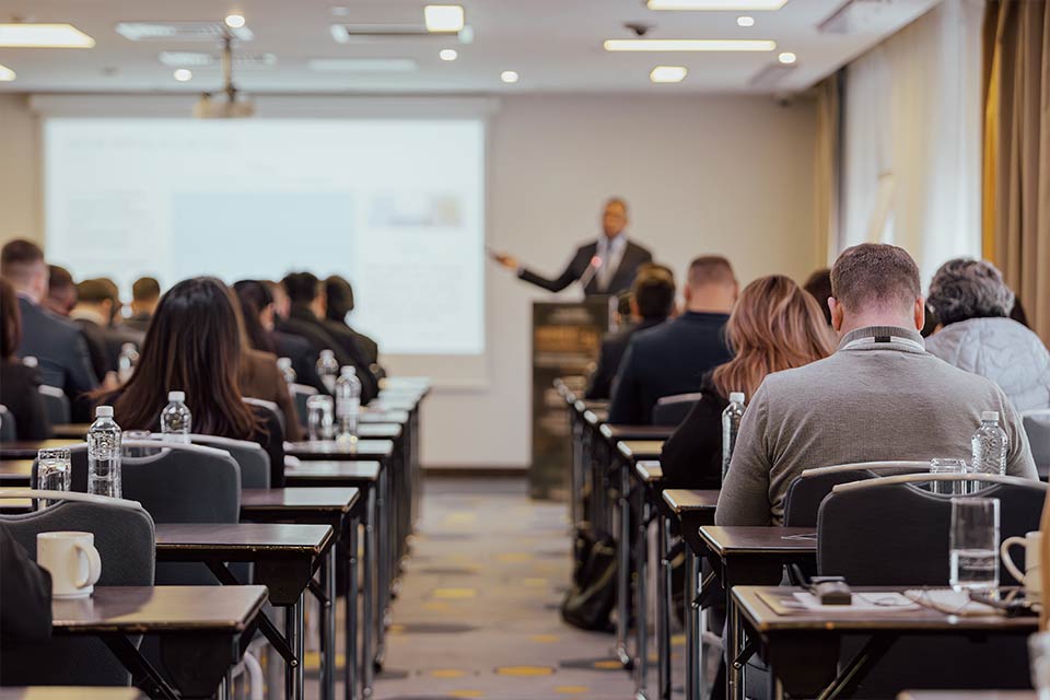 Many students sat at their desks in a classroom while a teacher is talking