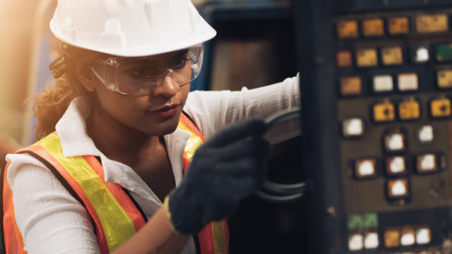 A person in a hard hat and safety glasses working on a piece of equipment