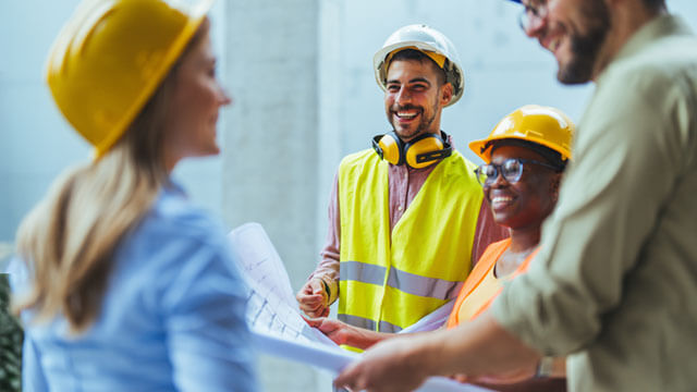 A group of people wearing hard hats and other safety equipment, smiling in conversation