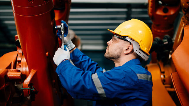 A person in a hard hat and overalls examining a piece of equipment