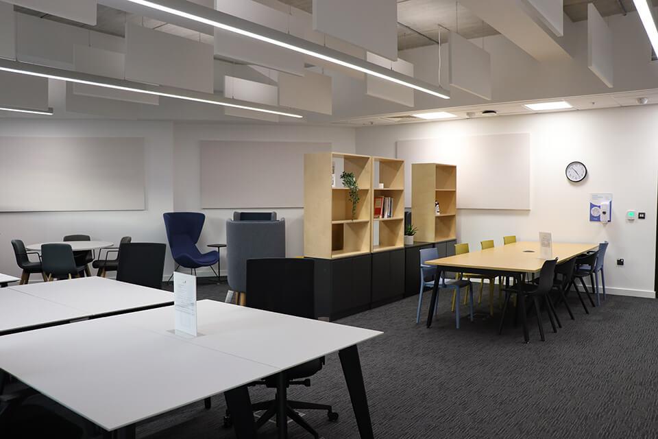 Photograph of the Keele University coworking space, foreground desks with chairs, background soft seating and bookshelves