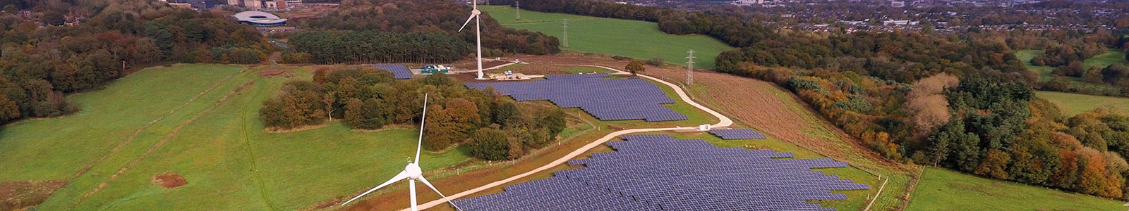 Drone photo of the Low Carbon Energy Generation Park during sunset, showing a field of solar panels and two wind turbines, at Keele University