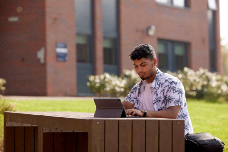 A student sat outside using a laptop