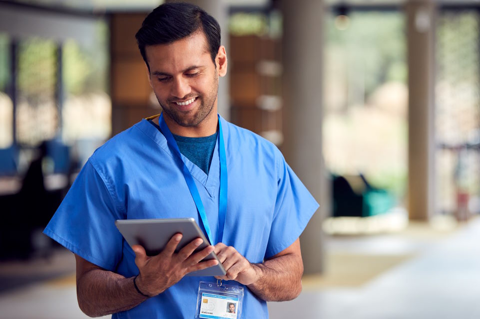 doctor, wearing scrubs, checking a computer tablet, in a hospital