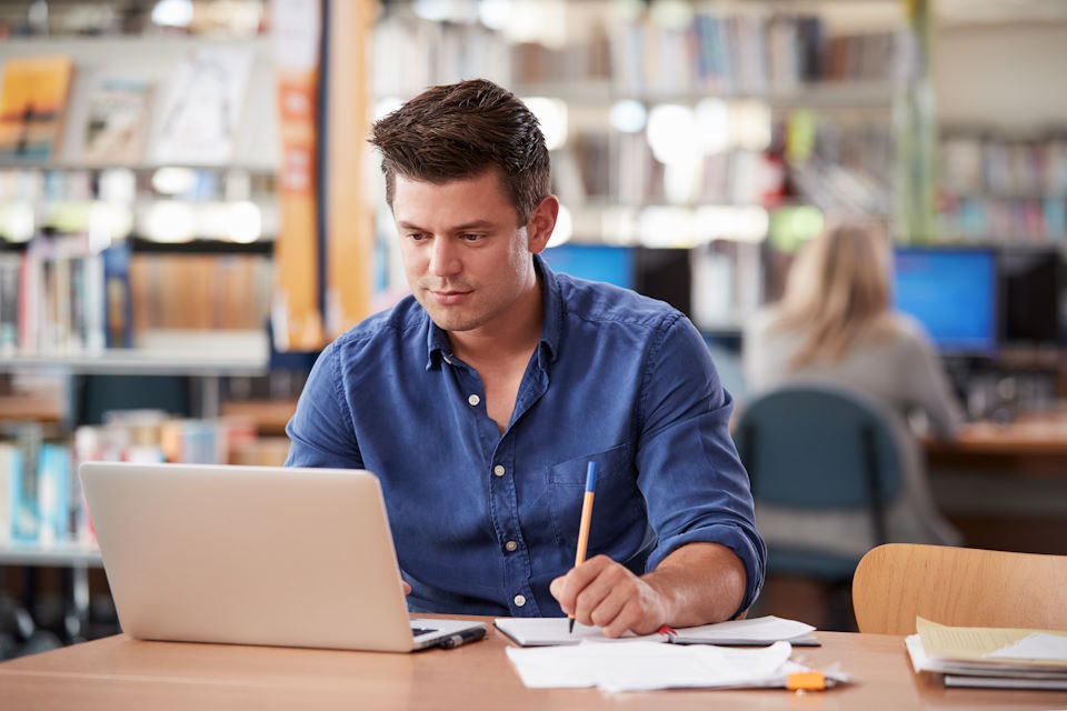academic studying in the library, using a laptop