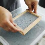 image of person holding a frame with pulp in it for paper making