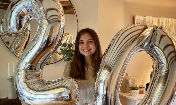 A young woman smiling with silver birthday balloons of the number 20.