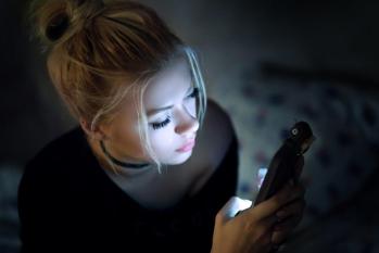 A young person sitting in the dark on their mobile phone.