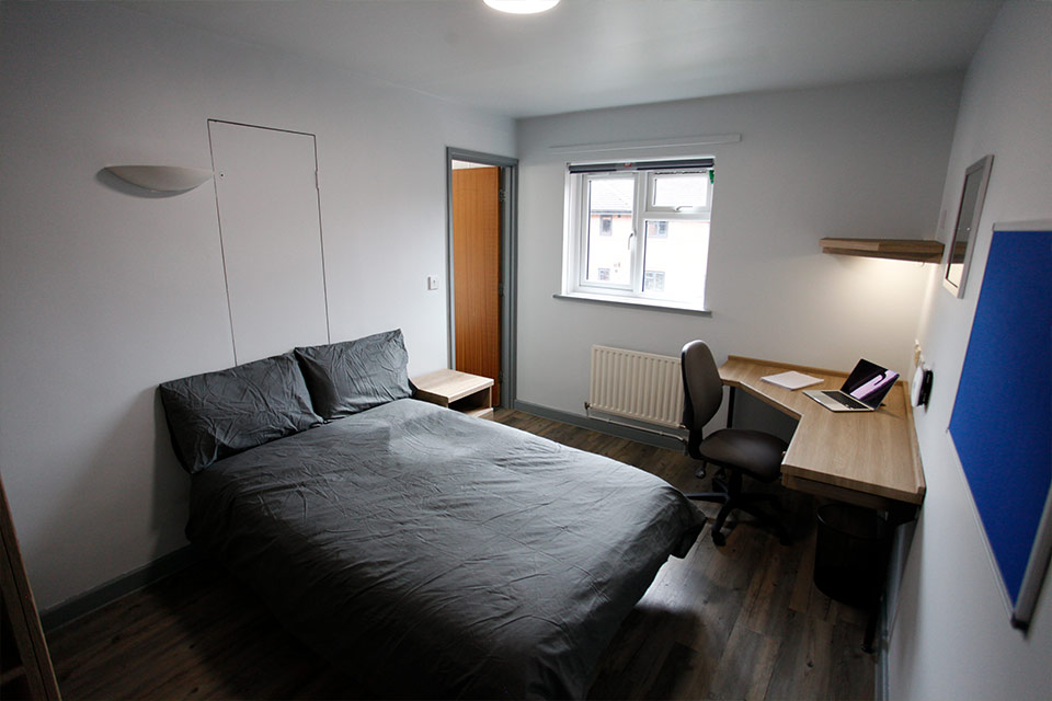 Interior of a student's bedroom decorated with a grey bed and blue pinboard.