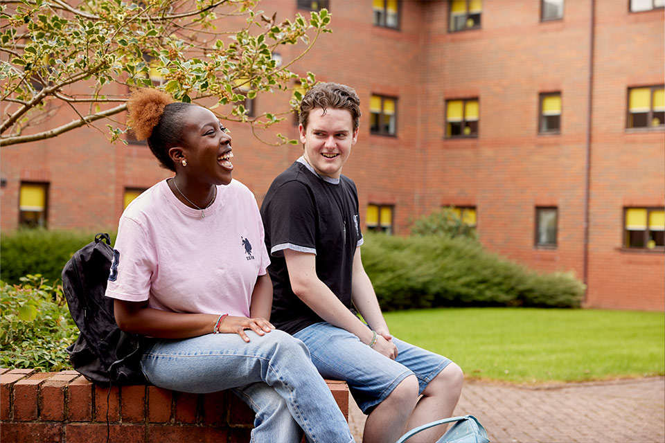 Two students laughing with each other, sat outside accommodation.