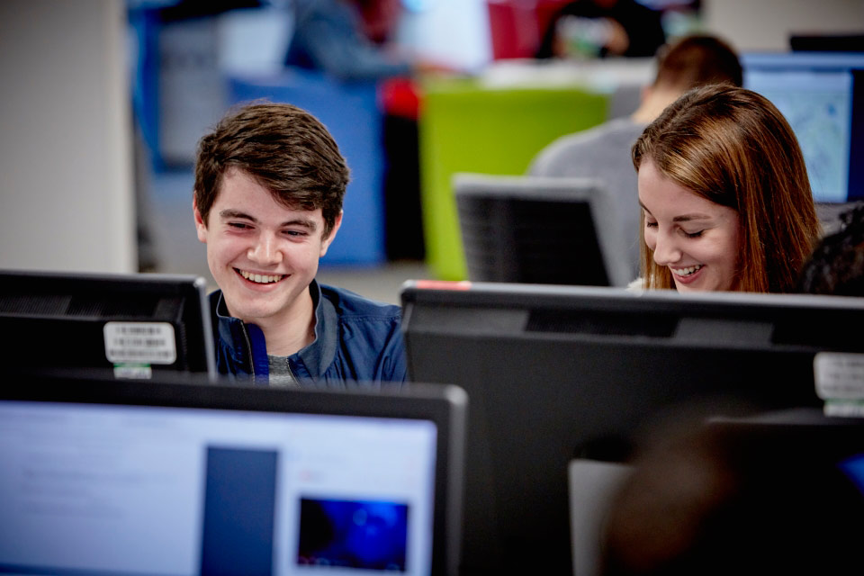 Students smiling, using computers in library on Keele campus