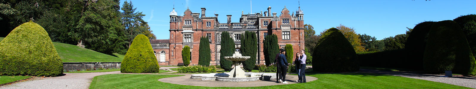 Keele Hall on a sunny day with a fountain in front of the building and four people stood talking