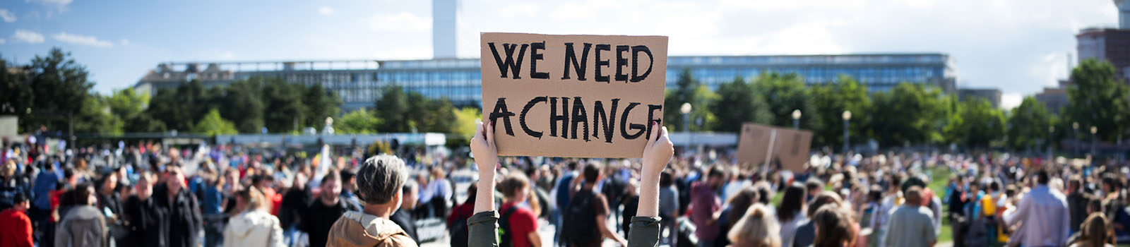 Image of crowd with individual holding a poster with text reading, 'we need a change'