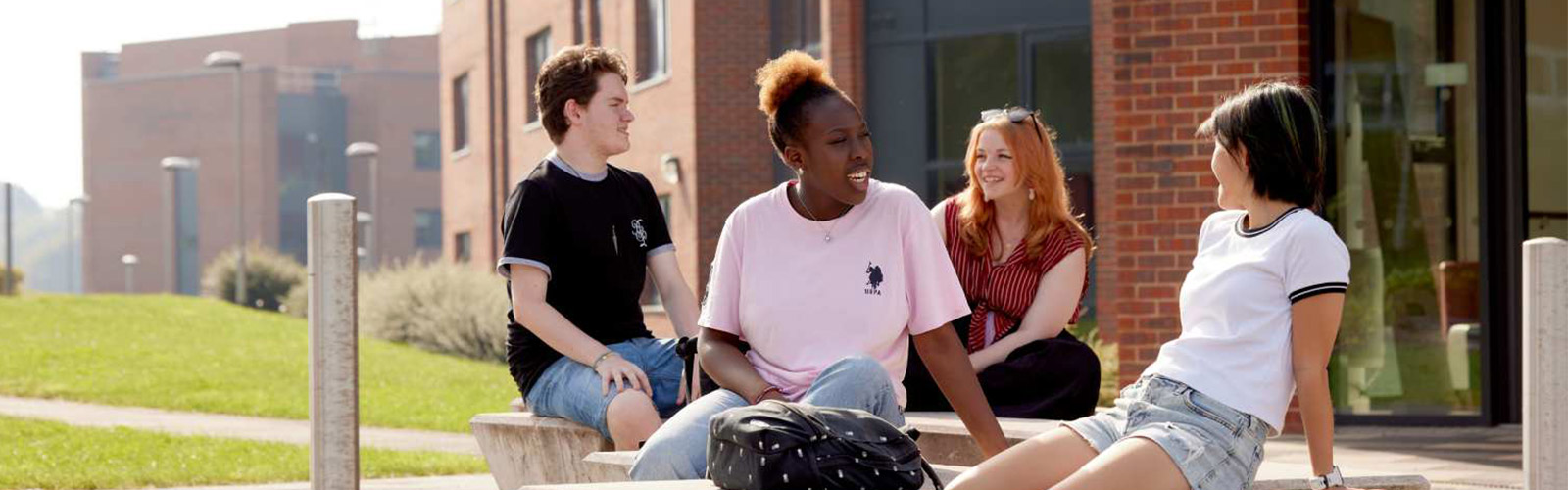 Four students sitting on stone pillars at Keele University
