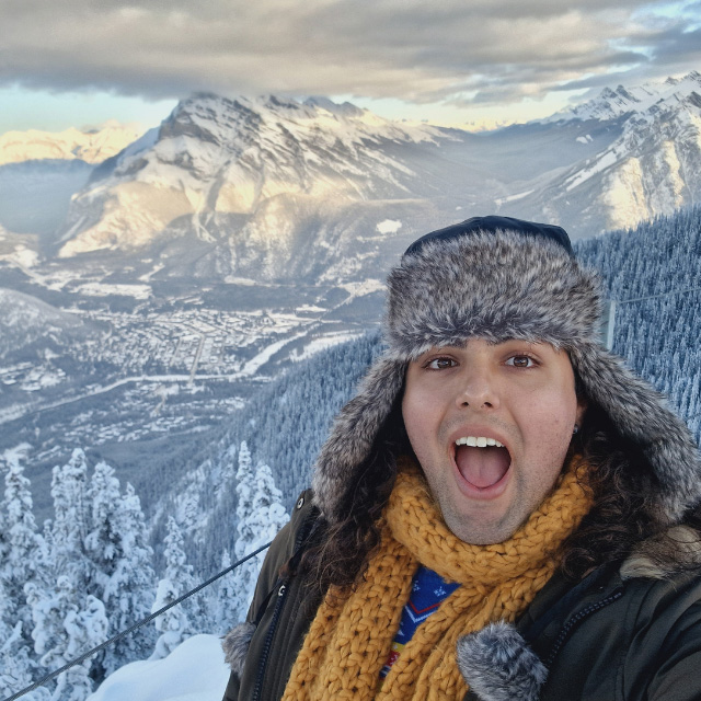 Person stood with their mouth open in front of a snow topped mountain range  
