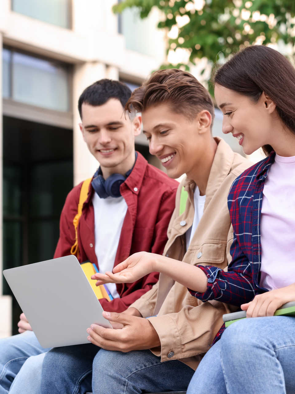 Three students sat looking at a laptop and talking with each other.
